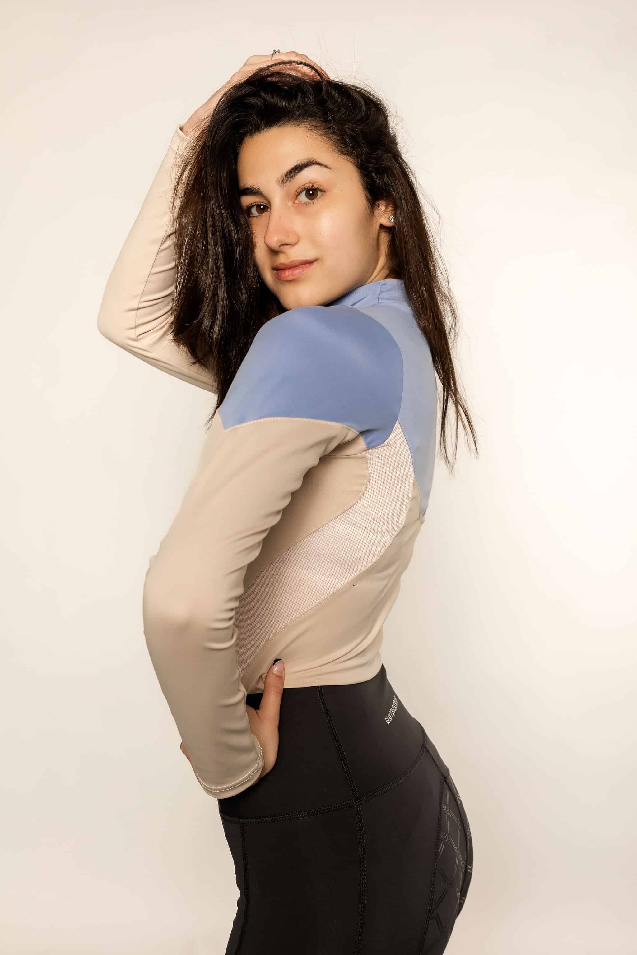 Model wearing a two tone equestrian base layer with 1/4 zip detail and mesh side panels with black riding leggings