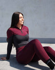 Brunette model wearing burgundy and grey base layer top with burgundy riding leggings sitting on the floor