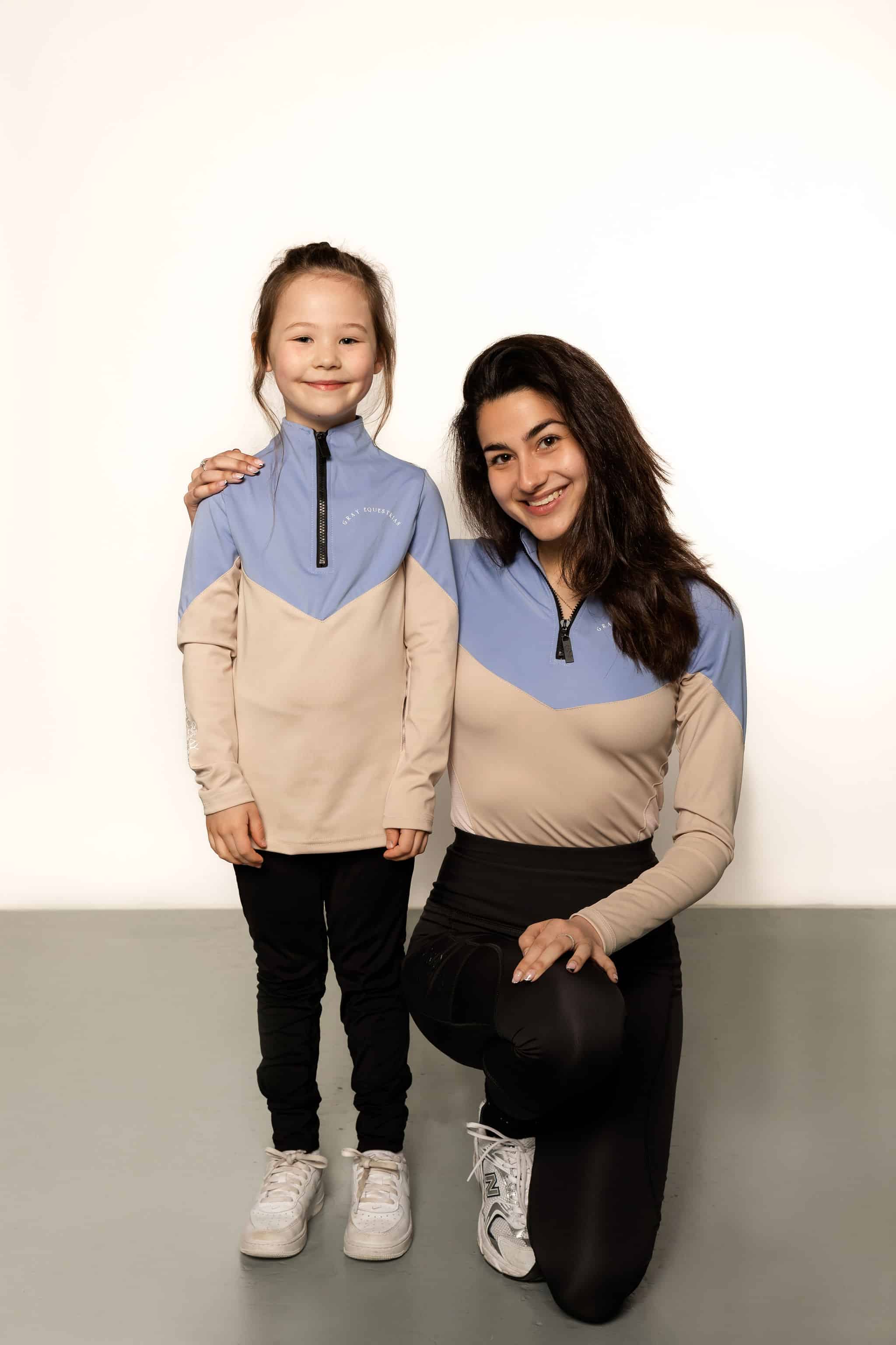Young rider and adult model wearing beige and blue base layer and riding leggings