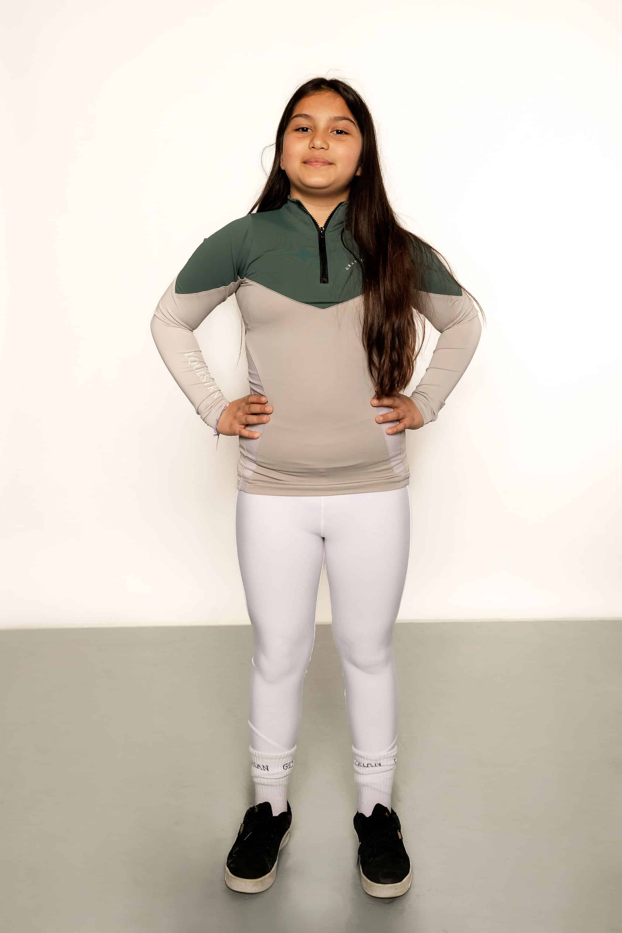 A child model wearing our our green and grey base layer with white leggings.