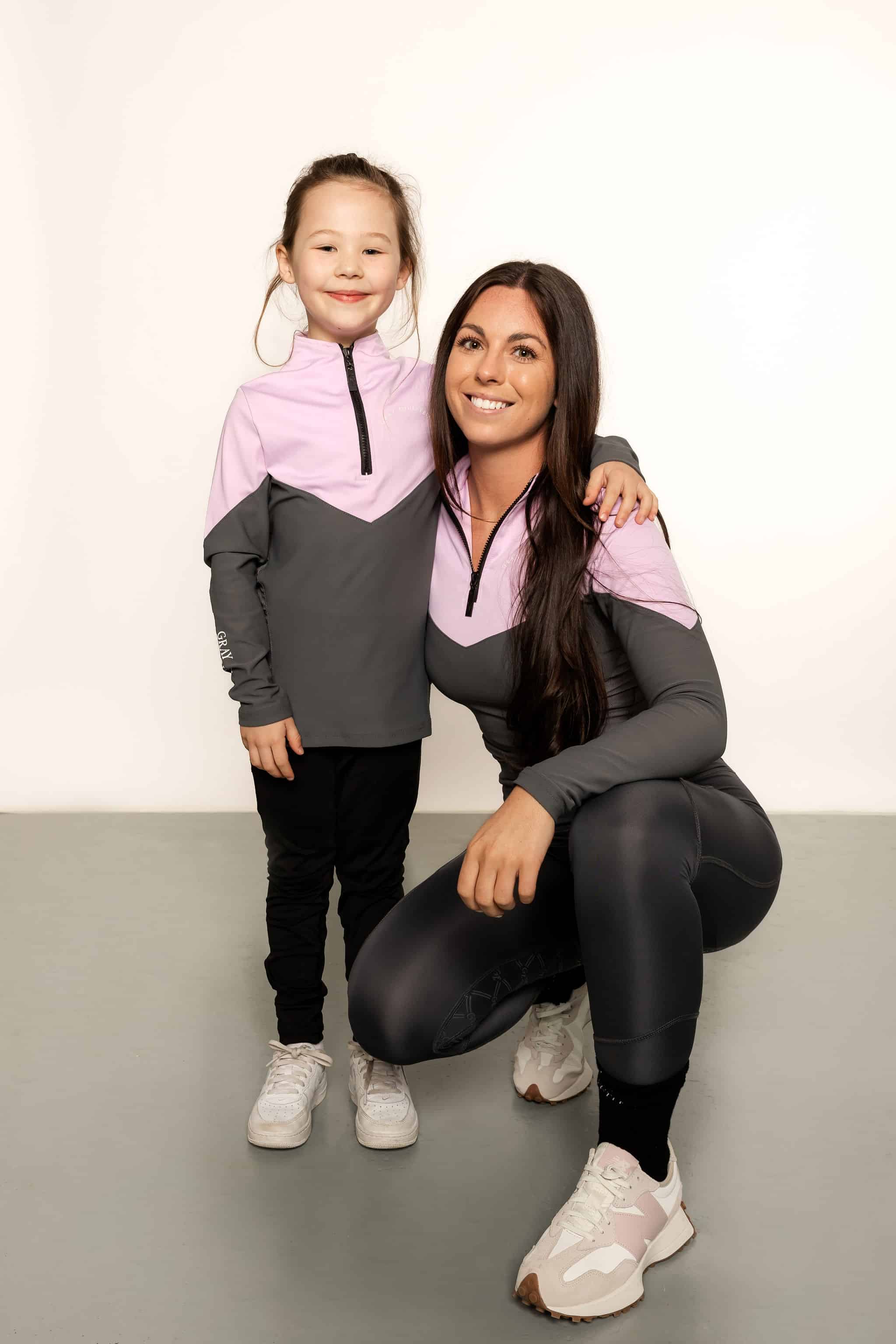 Young rider wearing lilac and grey base layer with adult rider bending down