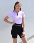 Brunette model wearing lilac short sleeved equestrian base layer with black 1/4 zip and black riding shorts