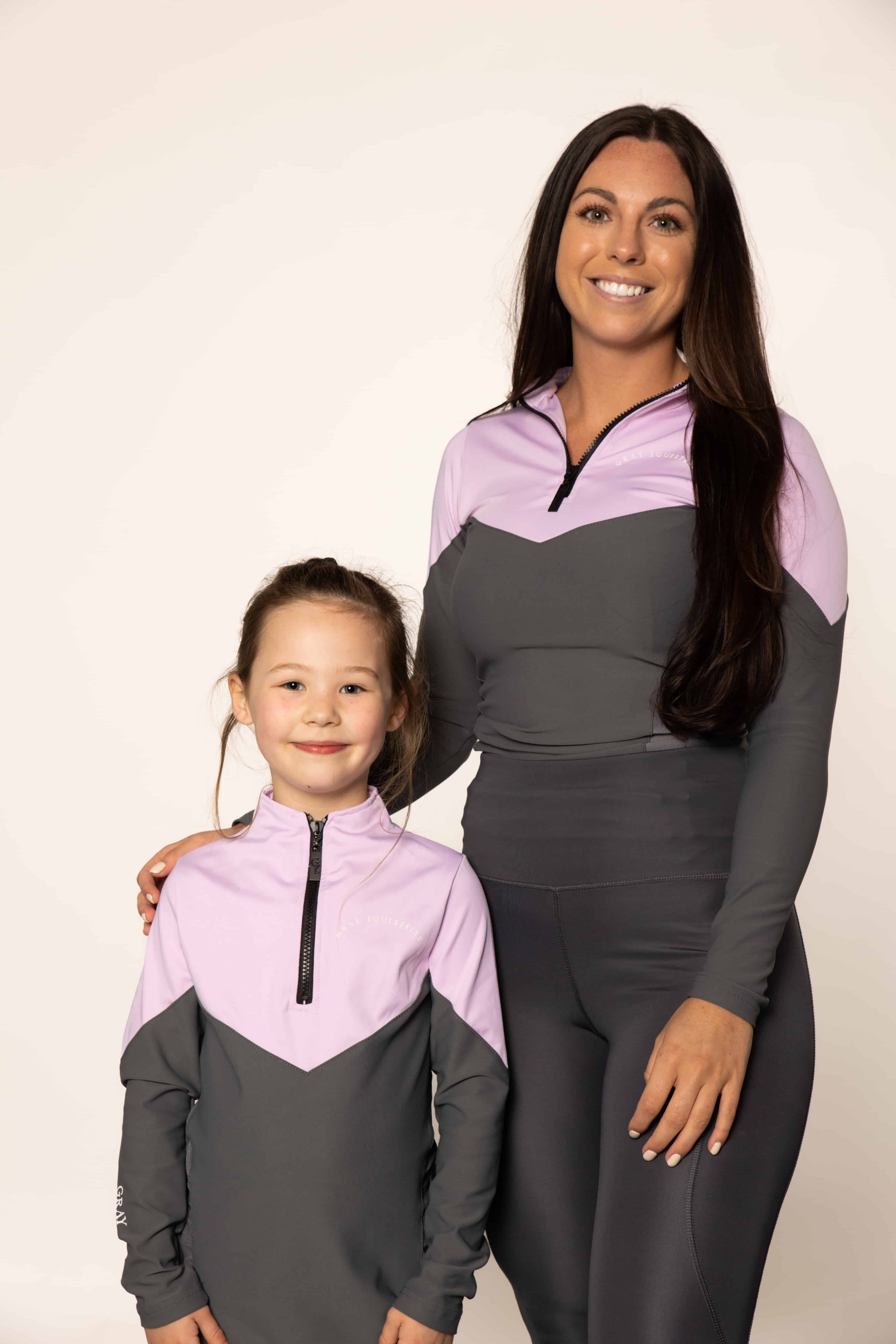 Two models, a young rider and an adult rider wearing the lilac and grey base layer top and grey leggings