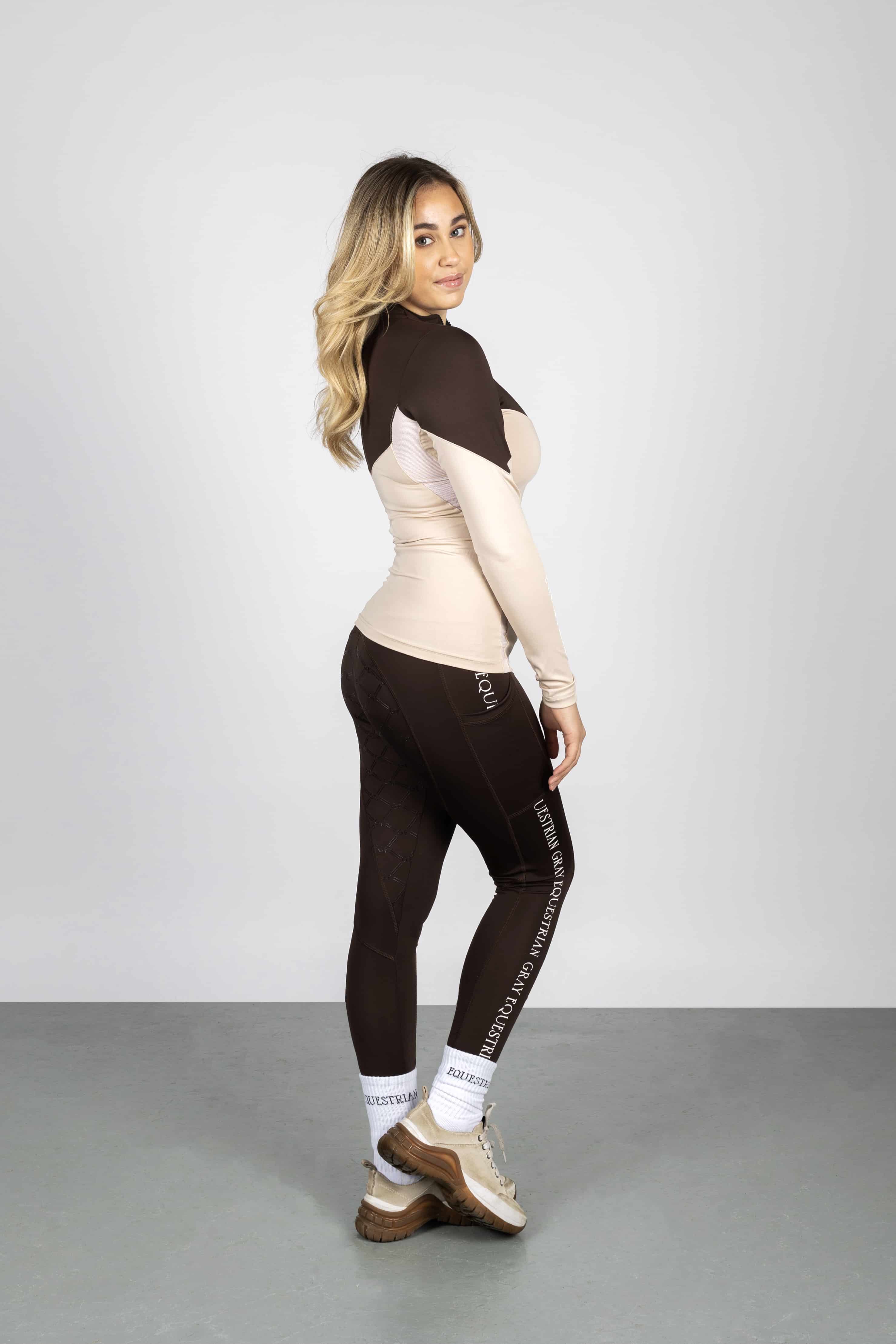 Model wearing a long sleeved brown and nude two toned base layer and brown equestrian leggings.