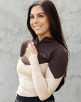 Model wearing a long sleeved brown and nude two toned base layer and black equestrian leggings.