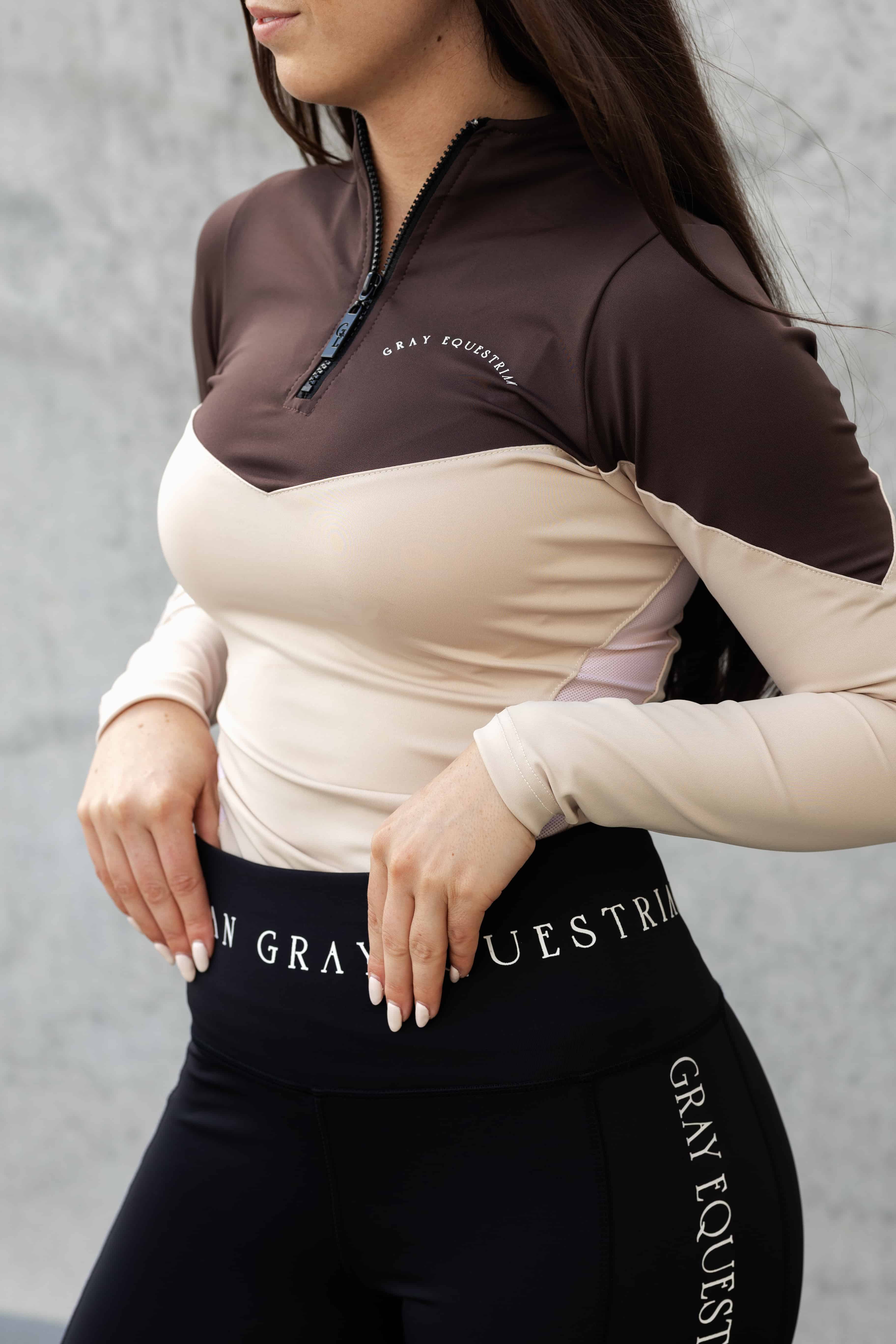 Model wearing a long sleeved brown and nude two toned base layer and black equestrian leggings.