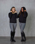 Two models standing side by side wearing our black fleece-lined oversized equestrian hoodie and grey riding leggings.