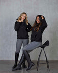 Two models standing side by side wearing our black fleece-lined oversized equestrian hoodie and grey riding leggings.