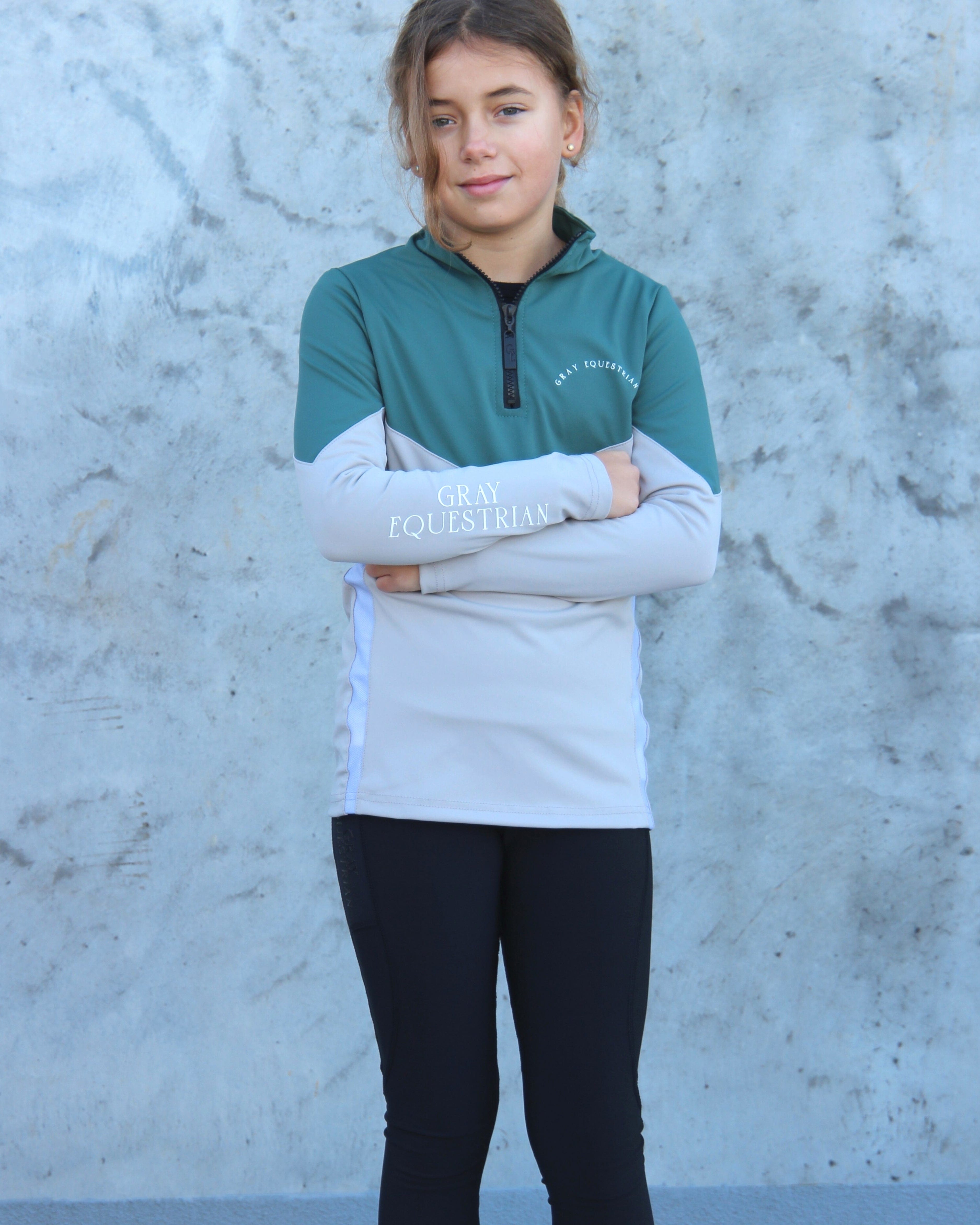 A child model wearing our our green and grey base layer with black leggings.