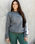 A model wearing our grey sweatshirt with white paneling down the sleeves and minimalist Grey Equestrian branding. The model is also wearing our green riding leggings.