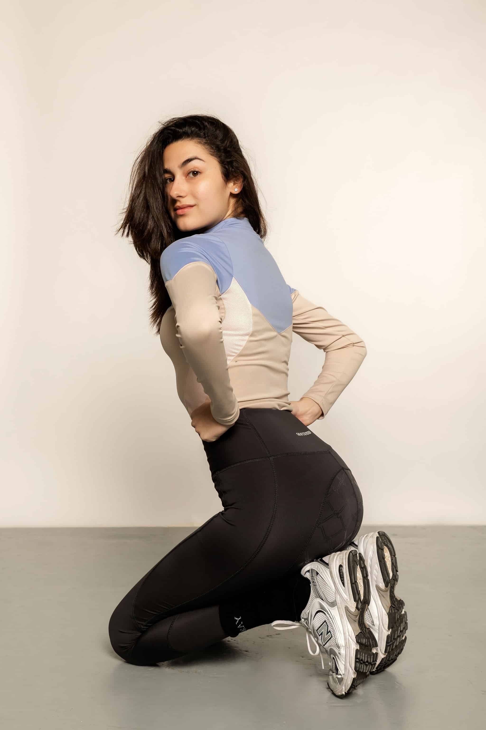 Model leaning down wearing blue & beige base layer with with black leggings.