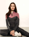 Model wearing charcoal grey riding leggings with pink and grey base layer top sitting down.
