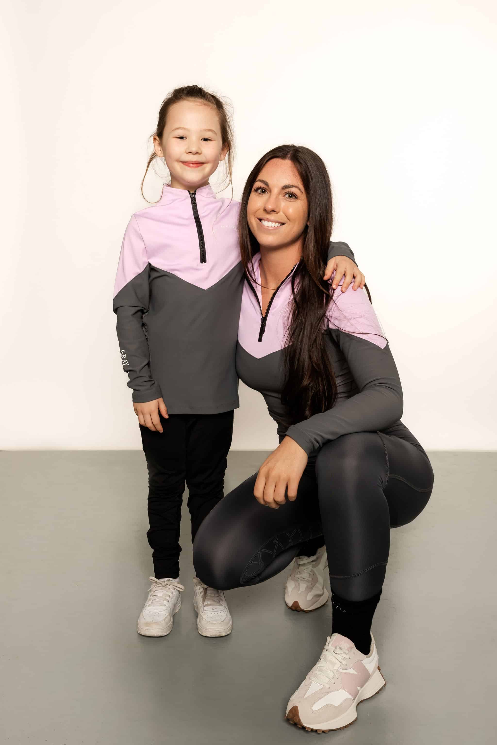 Young rider model and Model wearing charcoal grey riding leggings with pink and grey base layer top.