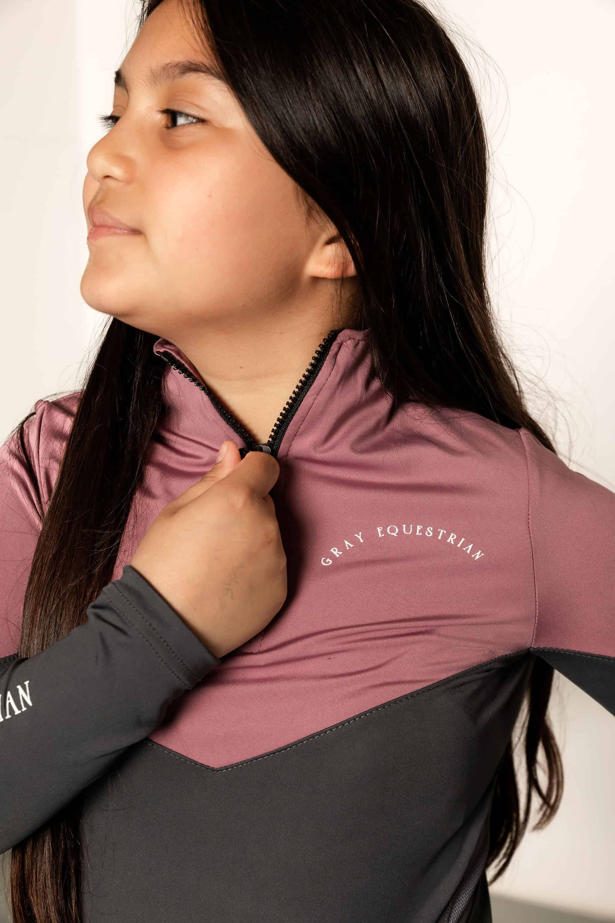 Young Rider holding 1/4 zip on pink and grey base layer