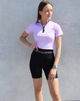 Brunette model wearing lilac short sleeved equestrian base layer with black 1/4 zip and black riding shorts