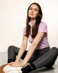 Brunette model sitting down wearing lilac short sleeved equestrian base layer with black 1/4 zip