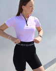 Brunette model wearing lilac short sleeved equestrian base layer with black 1/4 zip and black riding shorts