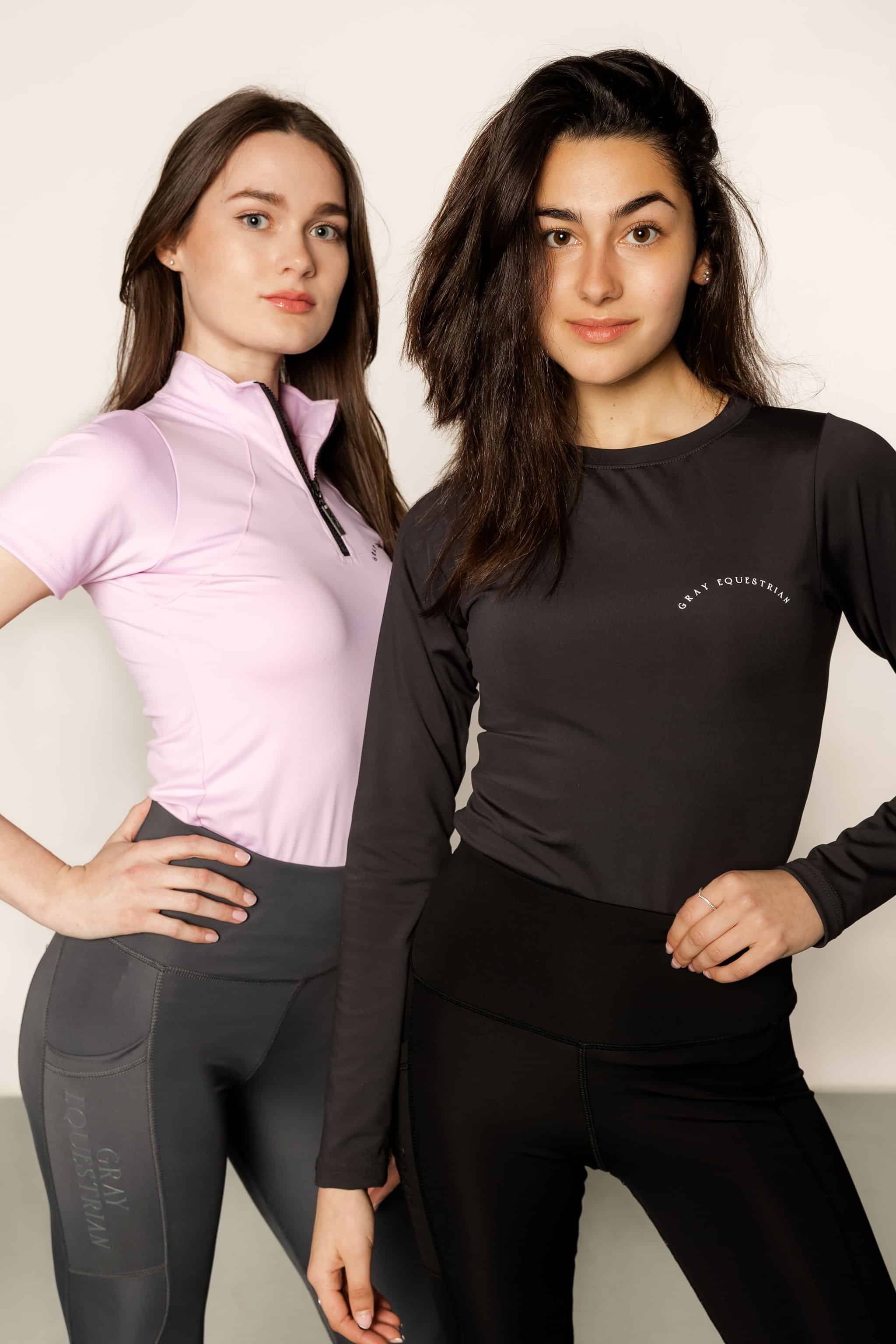 Brunette model wearing long sleeve equestrian lycra base layer top with model wearing lilac base layer and grey leggings