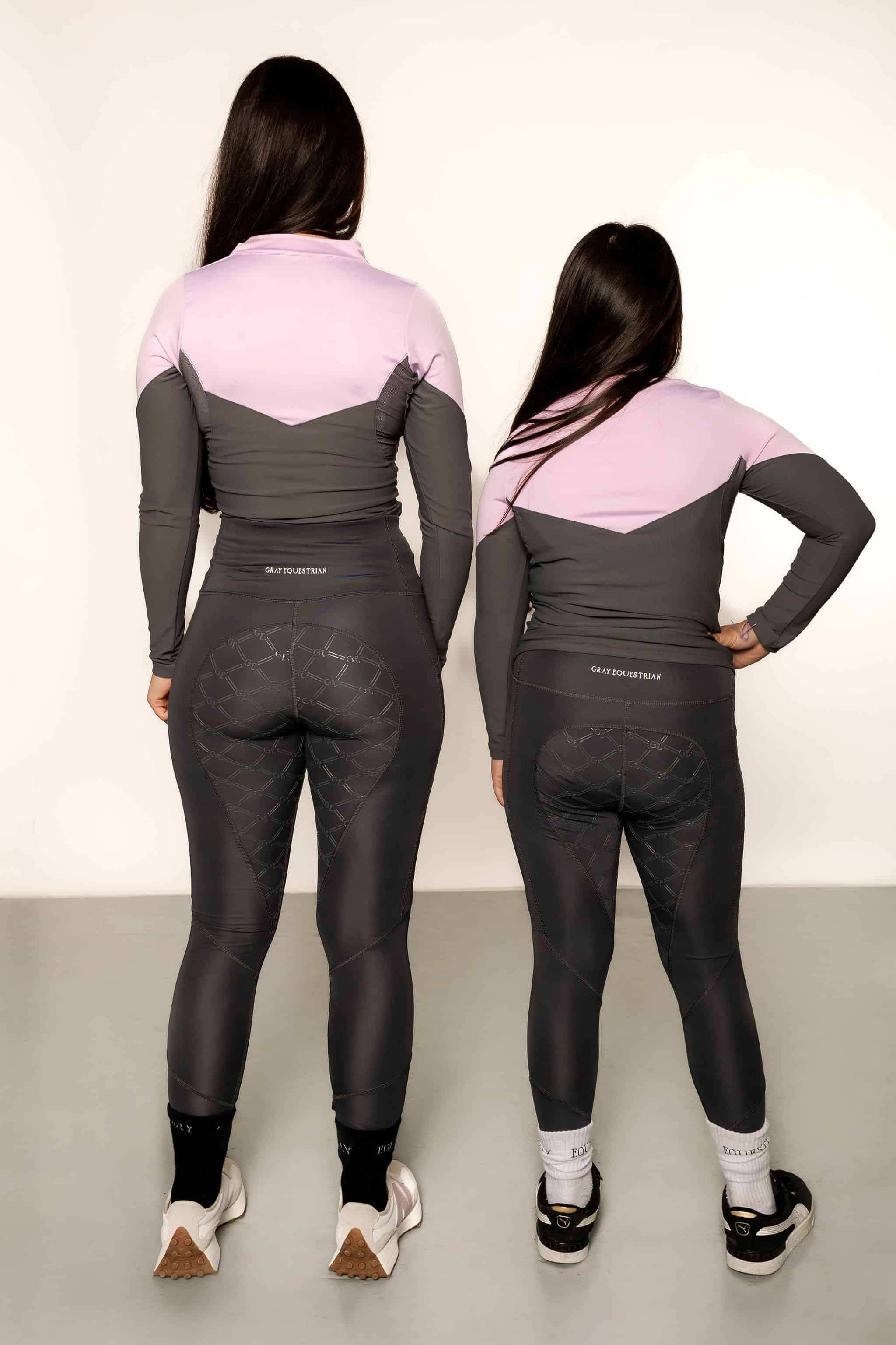 Two models, a young rider and an adult rider wearing the lilac and grey base layer top and grey leggings from behind 