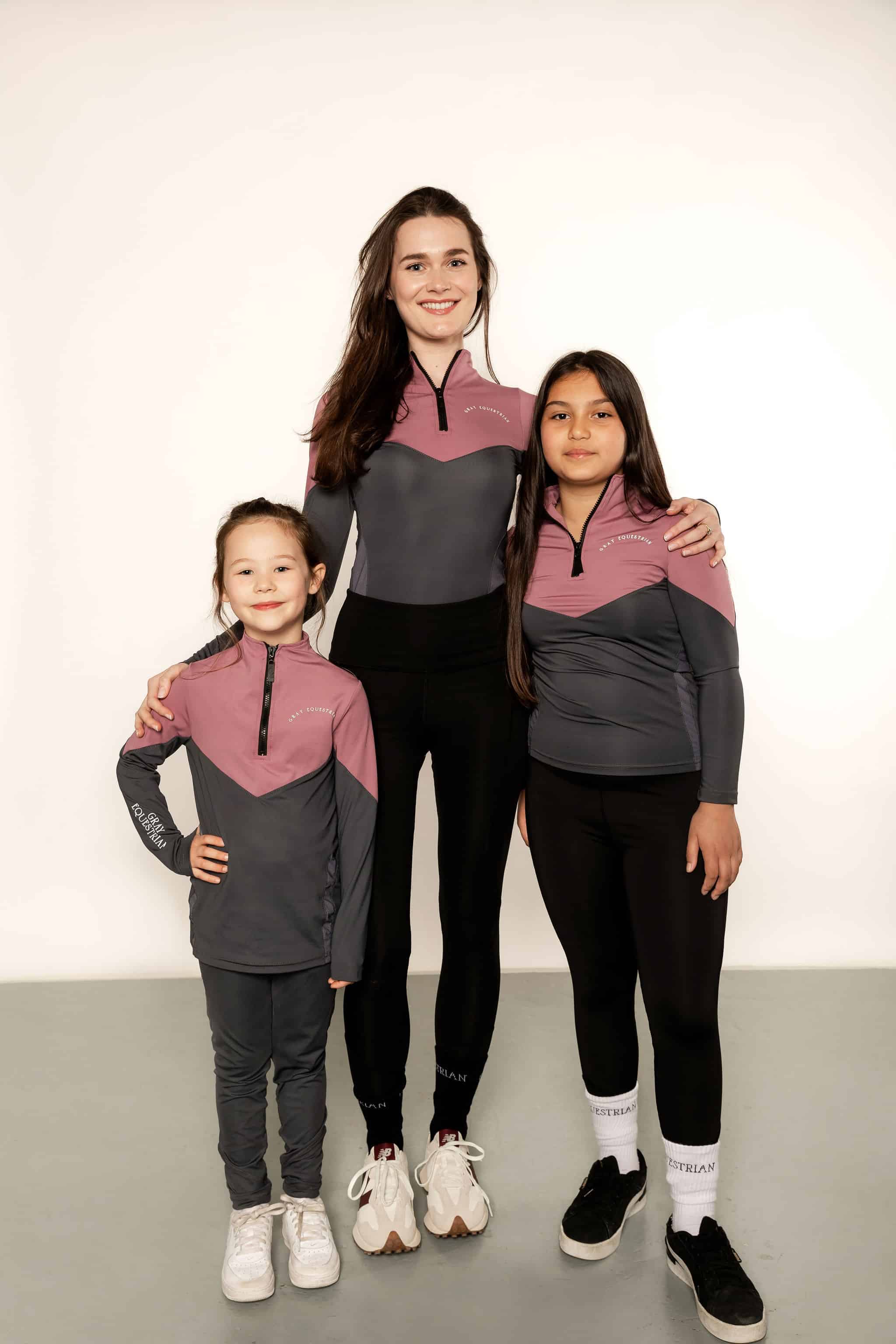 2 young riders and an adult rider in matching pink and grey sets.