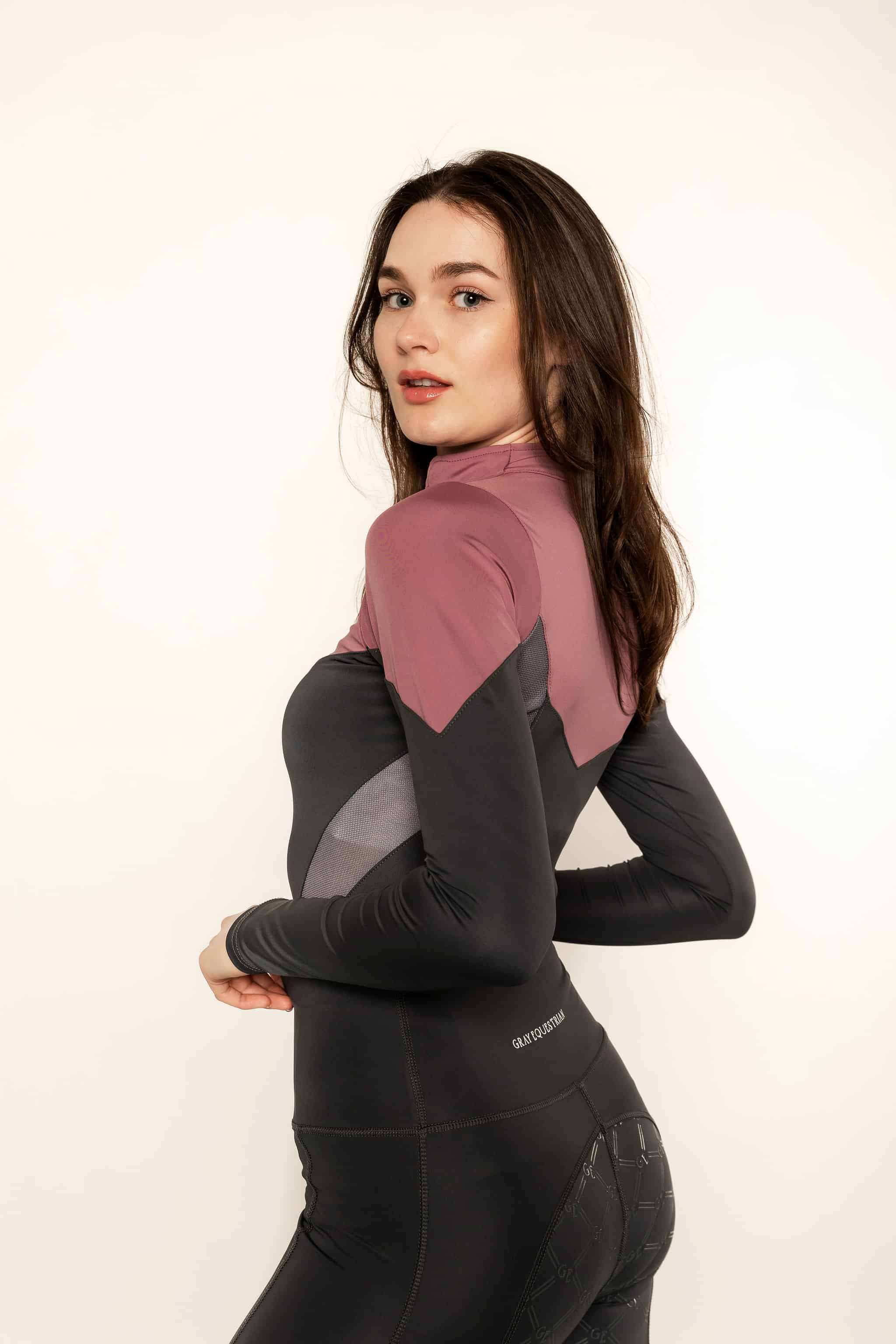 Brunette model wearing pink and grey base layer top and grey riding leggings.