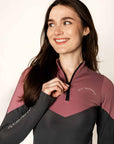 Brunette model wearing pink and grey base layer top while holding black 1/4 zip and grey riding leggings
