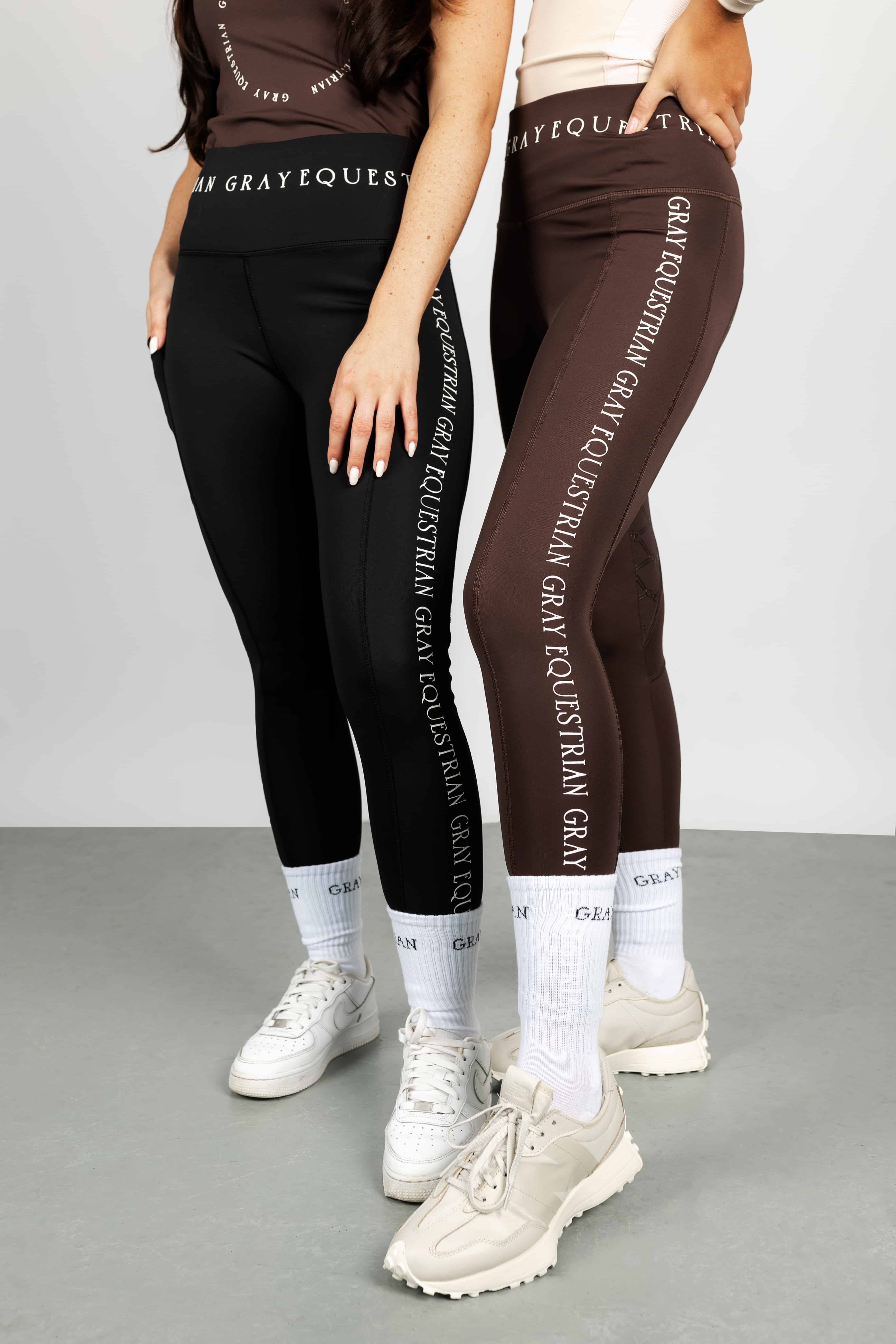 Two models standing next to each other. The model on the left is wearing our brown renew vest and black riding leggings. The model on the right is wearing our nude vest and brown renew leggings.