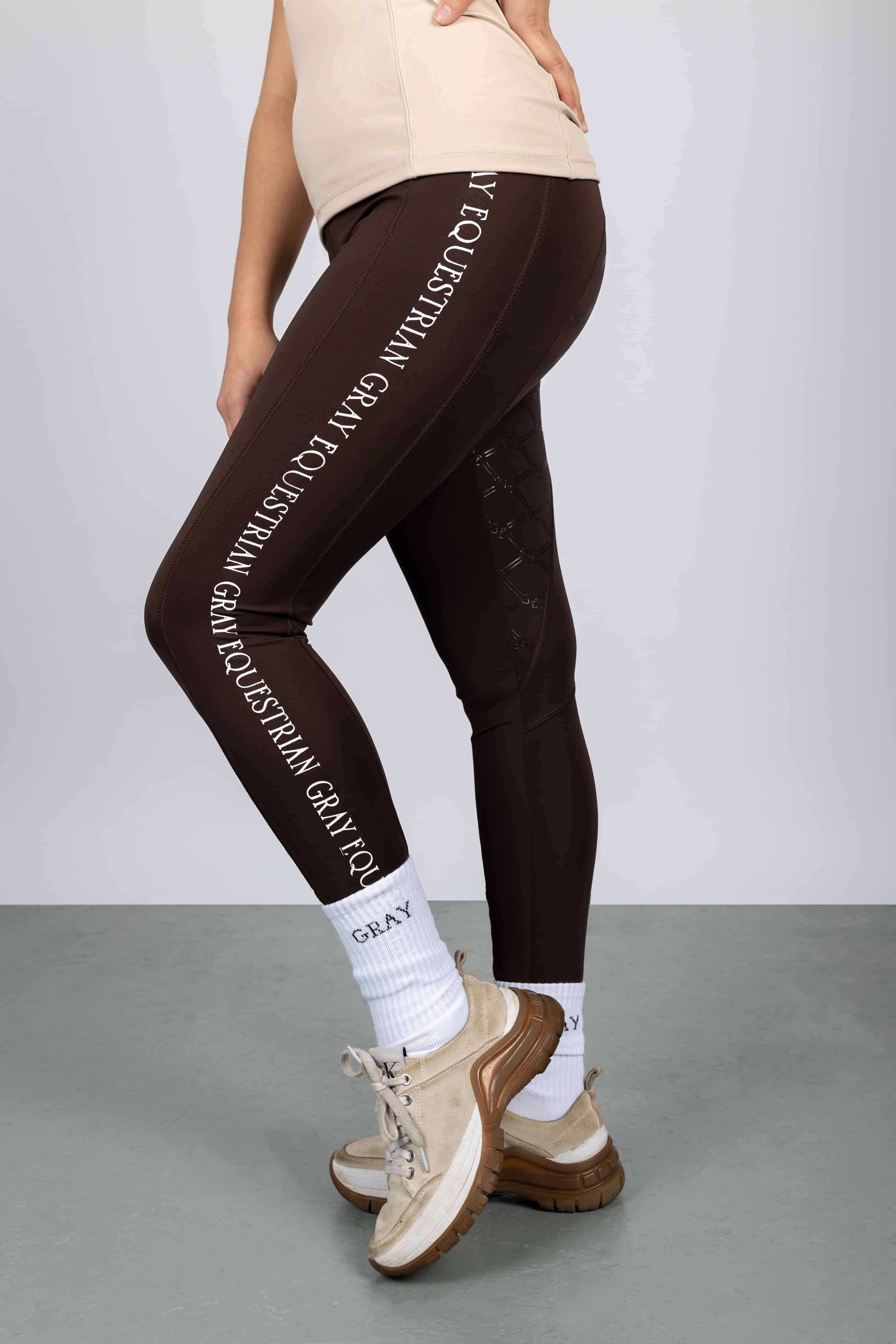 A model wearing our brown renew leggings with white Grey Equestrian branding down the side.