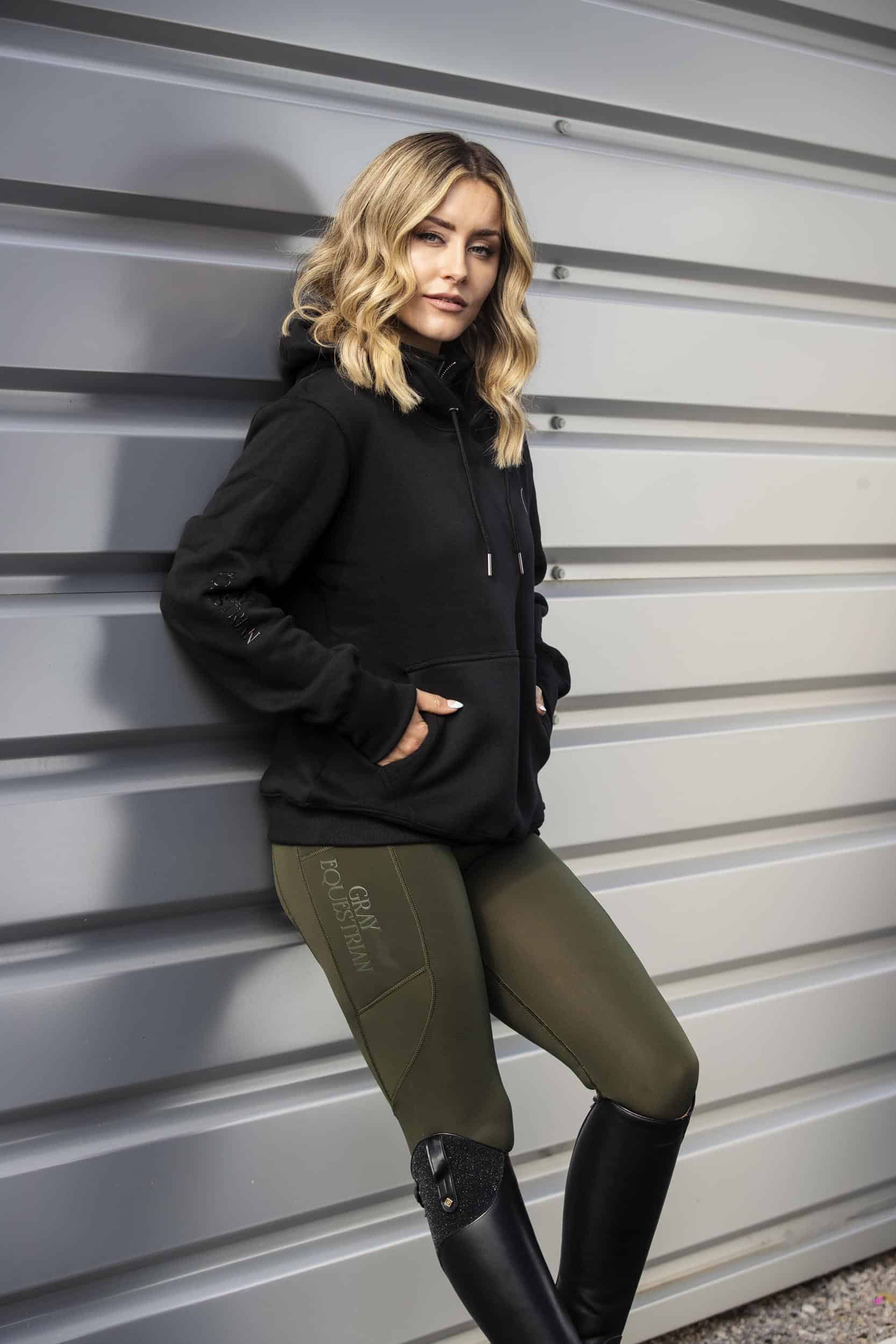 Blonde model wearing our black fleece-lined oversized equestrian hoodie and grey riding leggings.