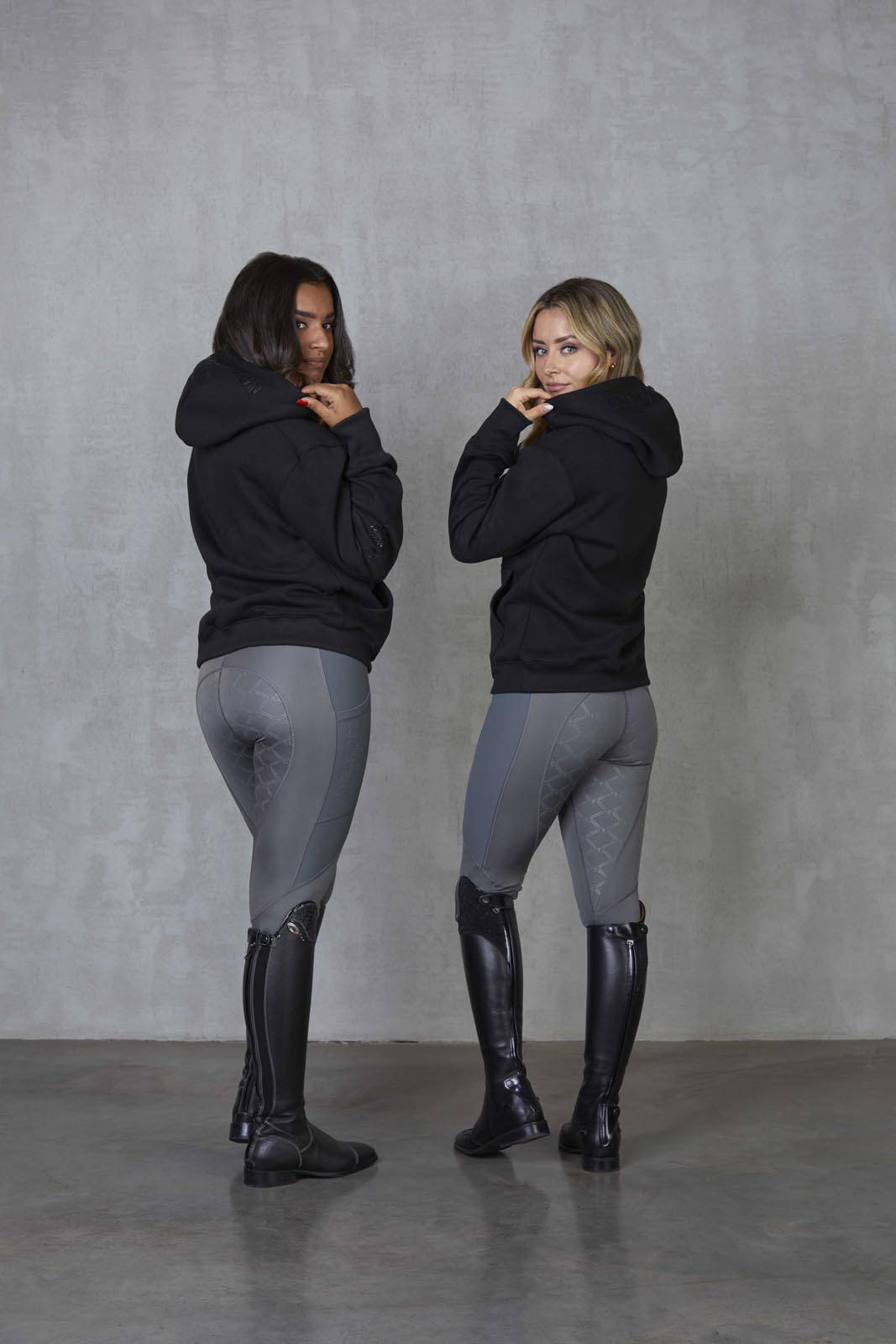 Two models standing side by side wearing our black fleece-lined oversized equestrian hoodie and grey riding leggings.