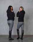 Two models standing side by side wearing our black fleece-lined oversized equestrian hoodie and grey riding leggings.