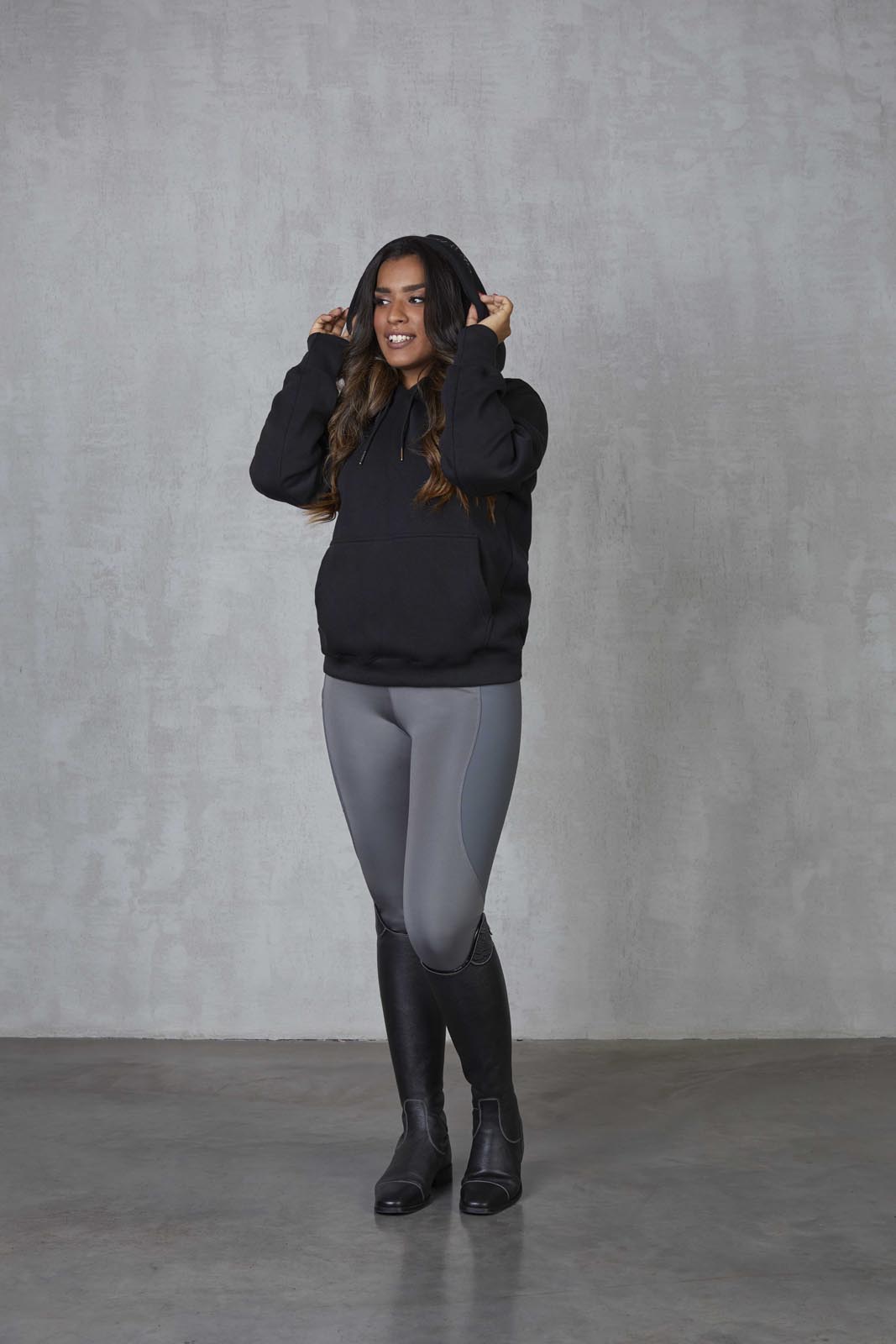 Brunette model wearing our black fleece-lined oversized equestrian hoodie and grey riding leggings.