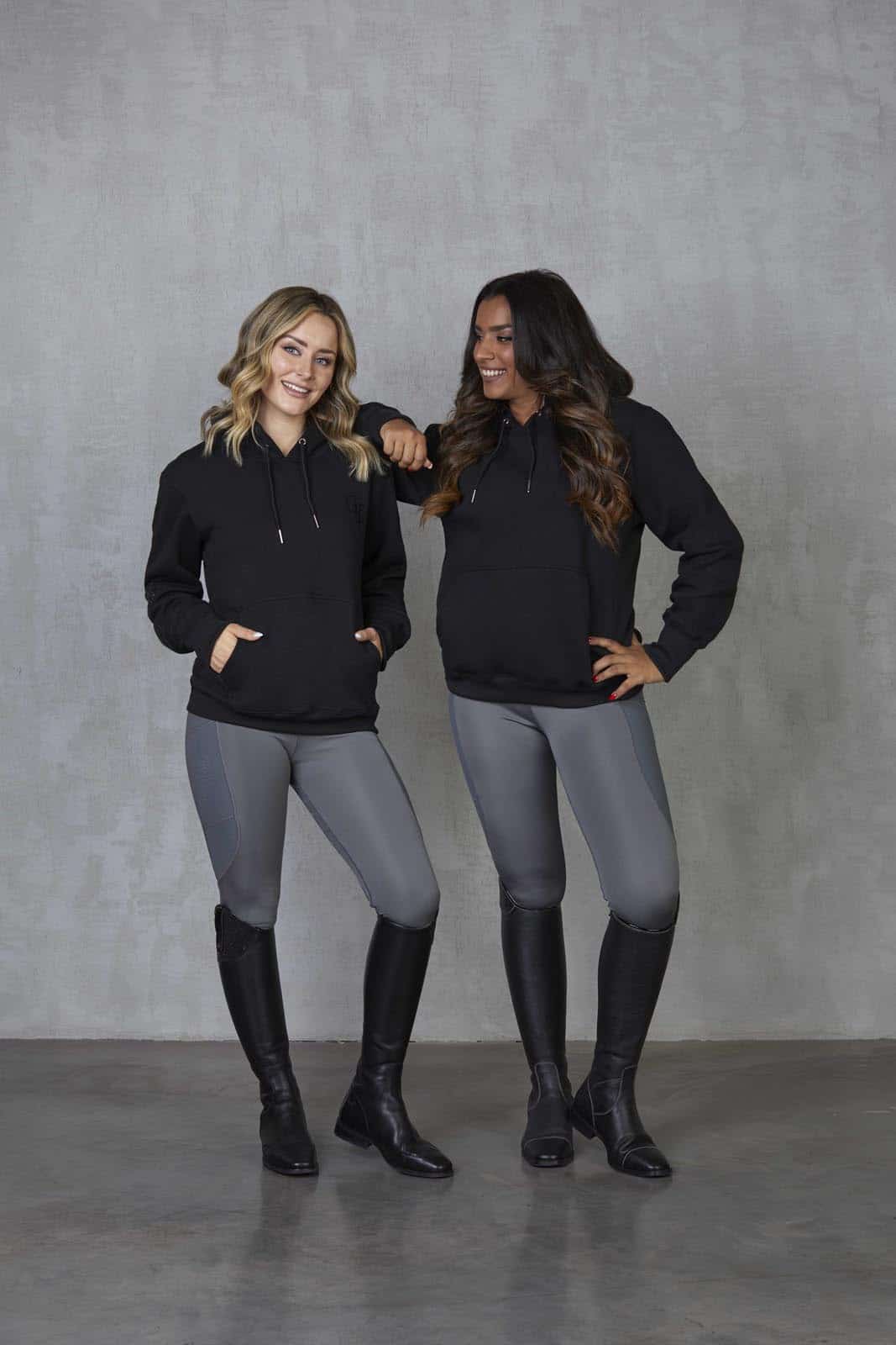 Two models standing side by side wearing our black fleece-lined oversized equestrian hoodie and grey riding leggings.