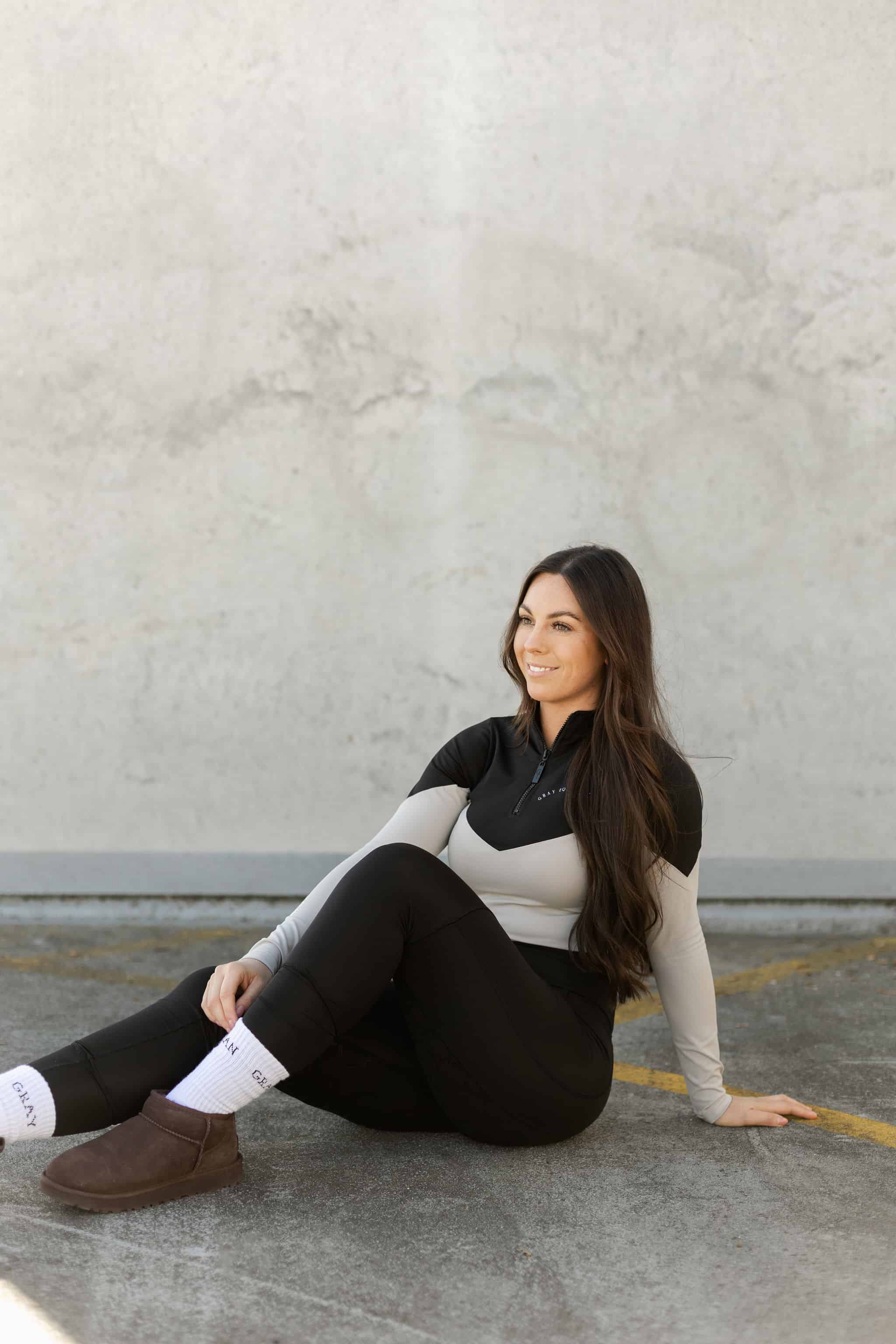 Brunette model wearing our long-sleeved black and grey two toned base layer and black equestrian leggings.