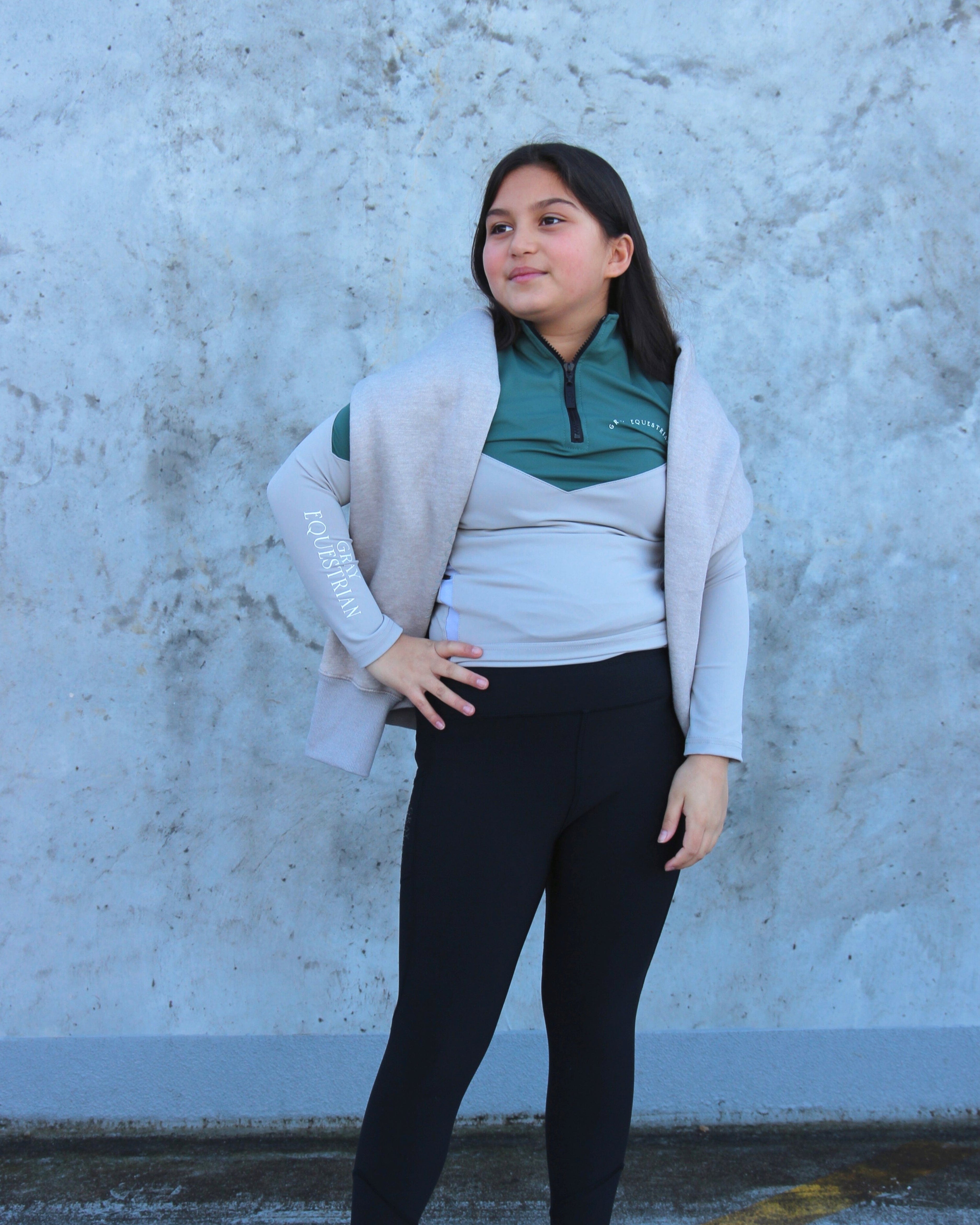 A child model wearing our our green and grey base layer with black leggings.