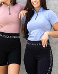 Two models standing next to each other. The one on the left is wearing our pink short sleeved base layer and riding shorts. The one on the right is wearing our light blue base layer and black riding leggings.