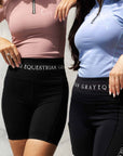 Two models next to each other. The model on the left is wearing a light pink short sleeved base layer and black riding shorts. The model on the right is wearing our light blue short sleeved base layer and black riding leggings.
