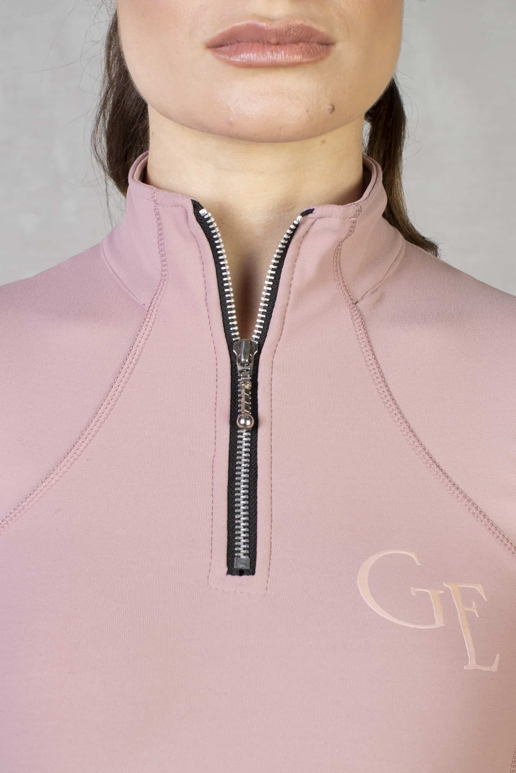 A close up of the silver 1/4 zip and subtle GE branding on our light pink short sleeved base layer.