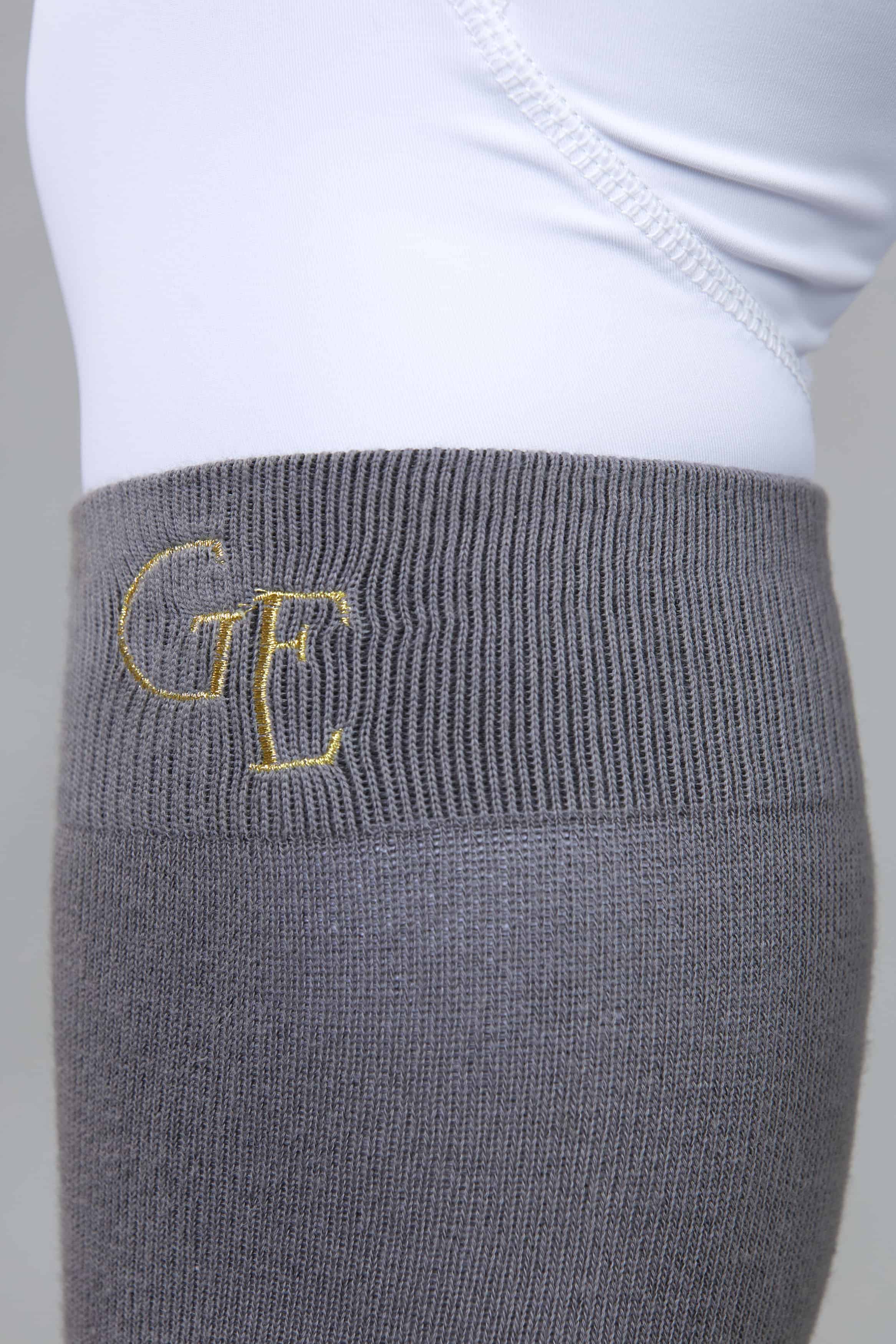 A close up of the gold G E logo on the top of our grey equestrian socks.